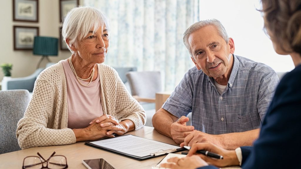 A senior couple is seated at a table with a care administrator during a counseling session.